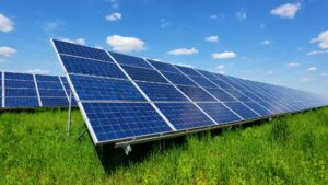 Solar panel on blue sky background. Green grass and cloudy sky. Alternative energy concept